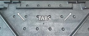 Close-up of textured metal surface with circular indentations and highlighted rectangular tabs, showing alignment features for assembly or installation.